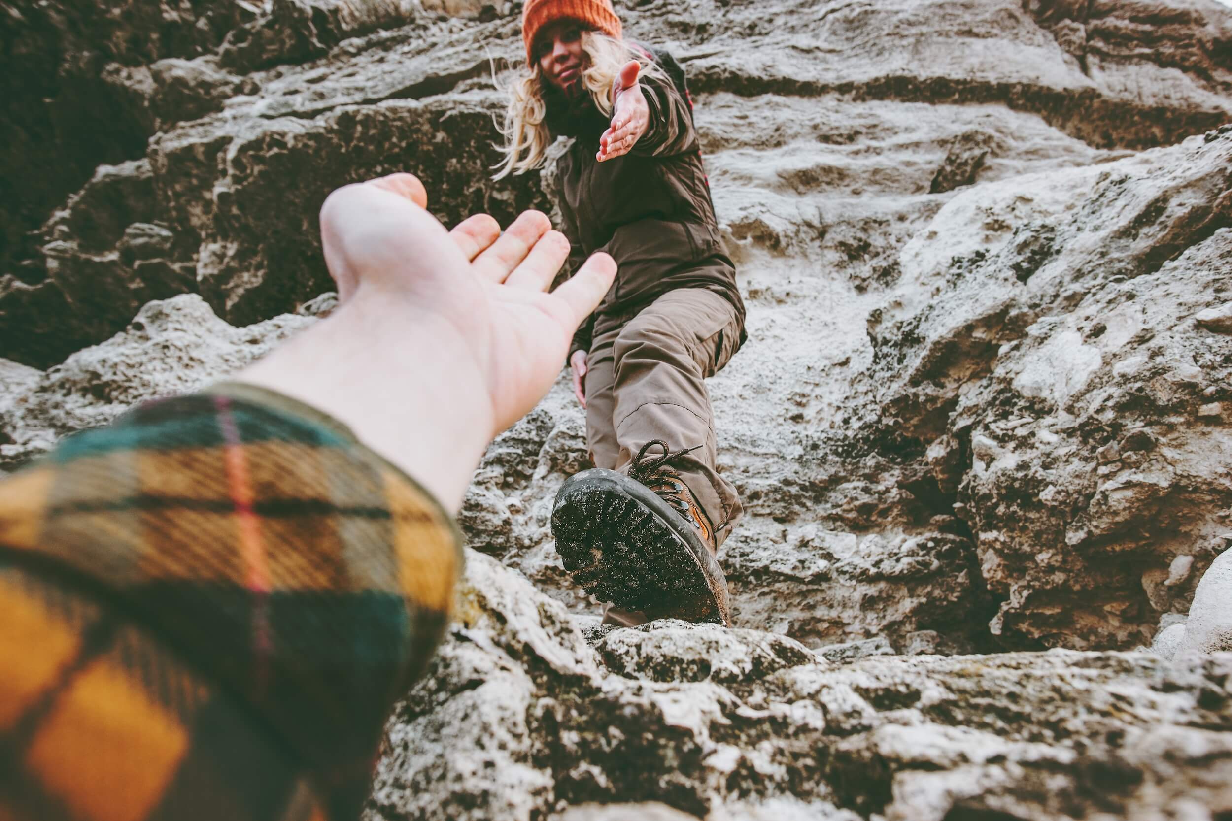 Trust with clients. Couple climbing mountain with hand out to help climb up.